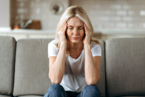 woman sitting on couch in pain from a sinus headache or a migraine